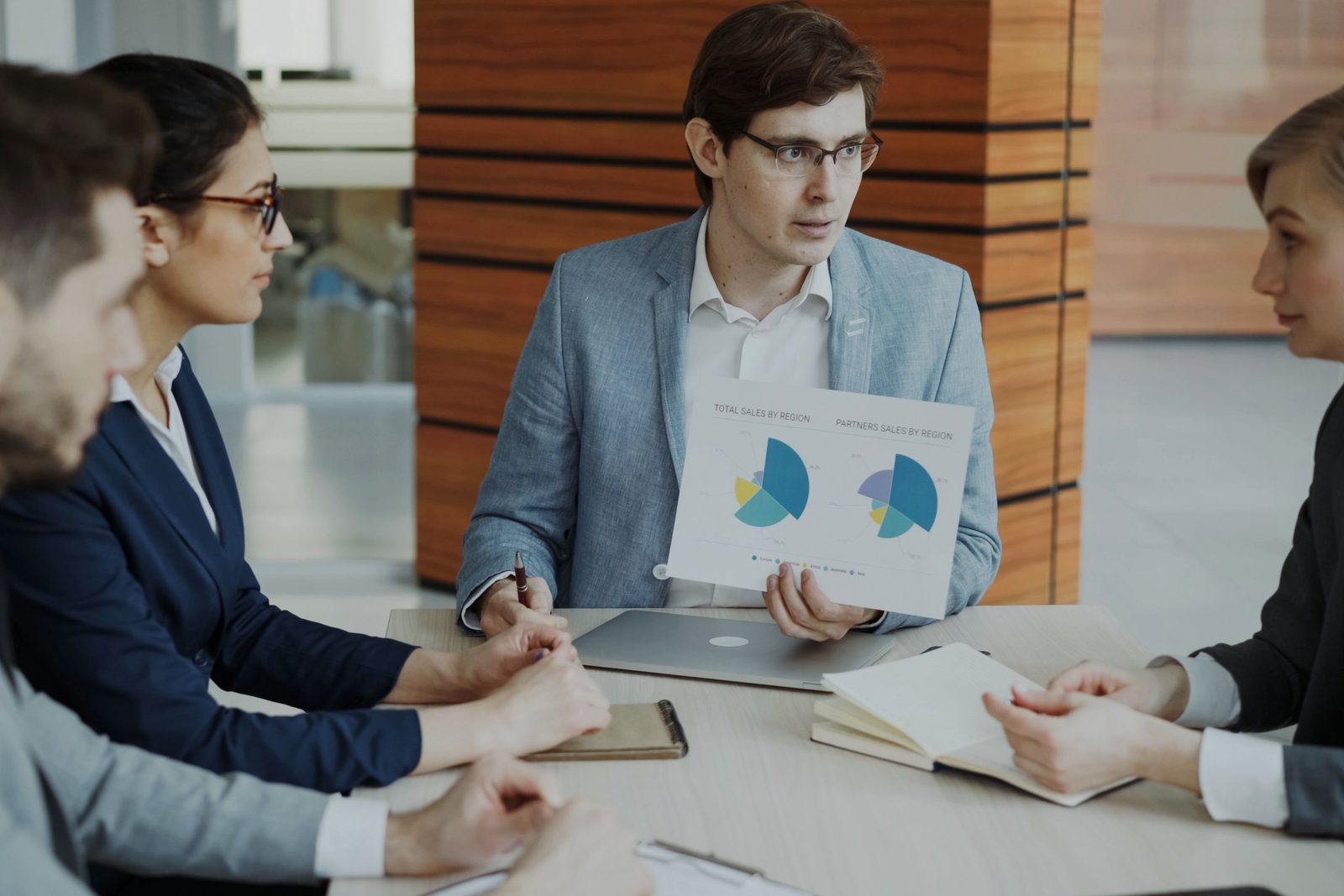A small group in a meeting room follows a colleague explaining a chart