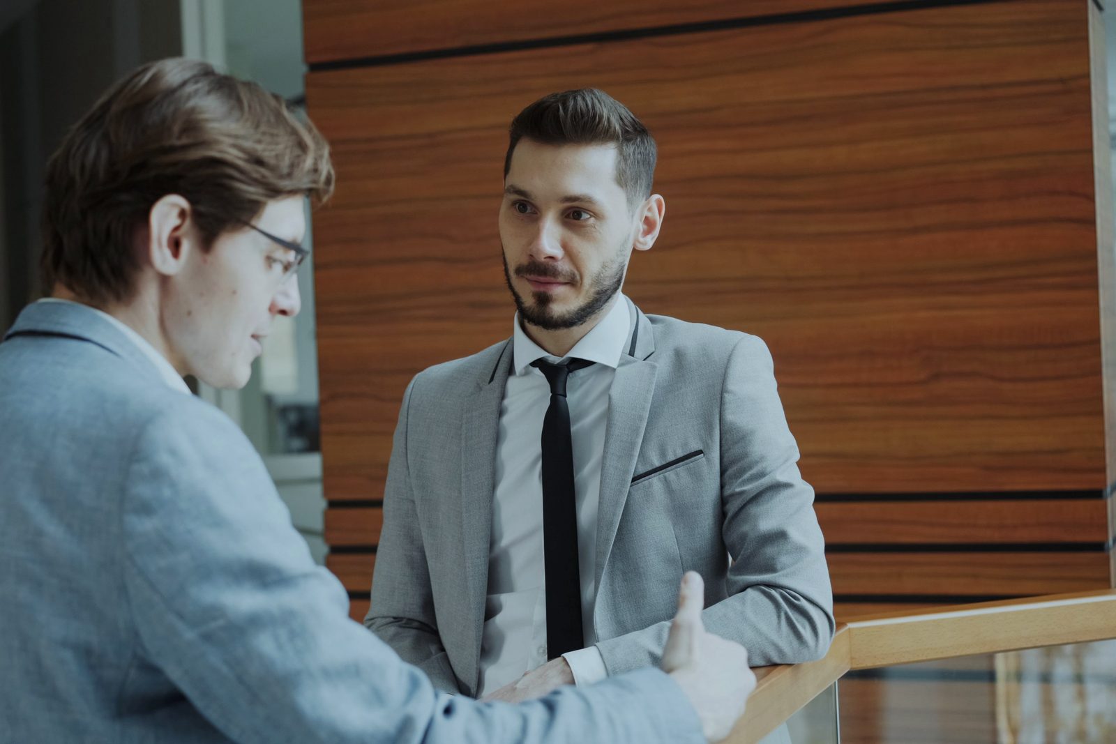 Two colleagues in jackets talk and listen to each other in a bright office