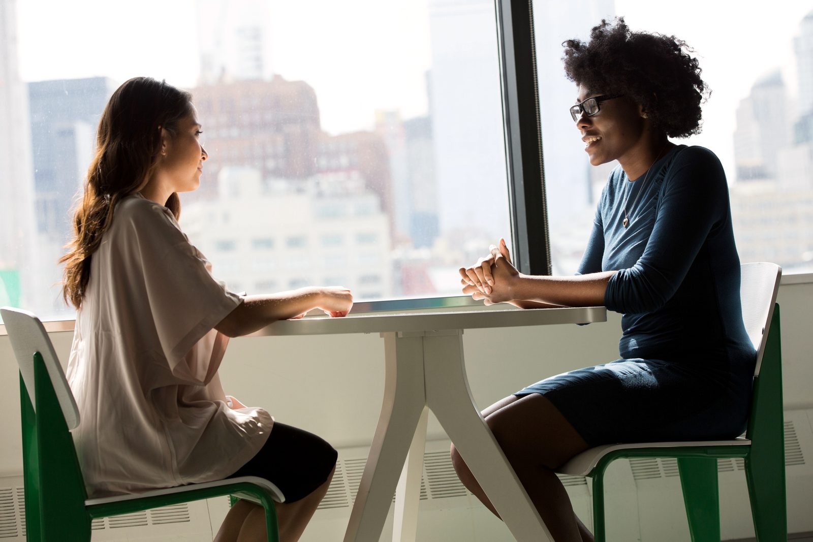 Two colleagues talk, seated by a large window