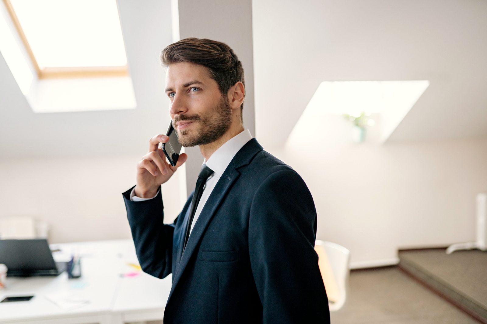 A professional in a navy suit on the phone with a customer, in a bright office